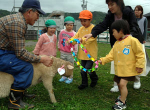 子羊に手づくりの首飾りをプレゼントする園児たち